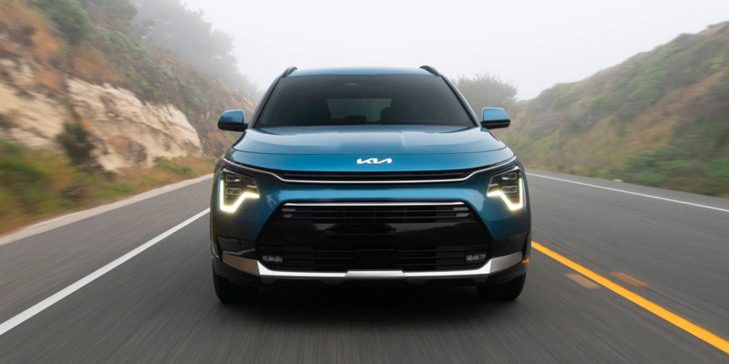 the front end of a blue 2025 Kia Niro Plug-In Hybrid driving down a road